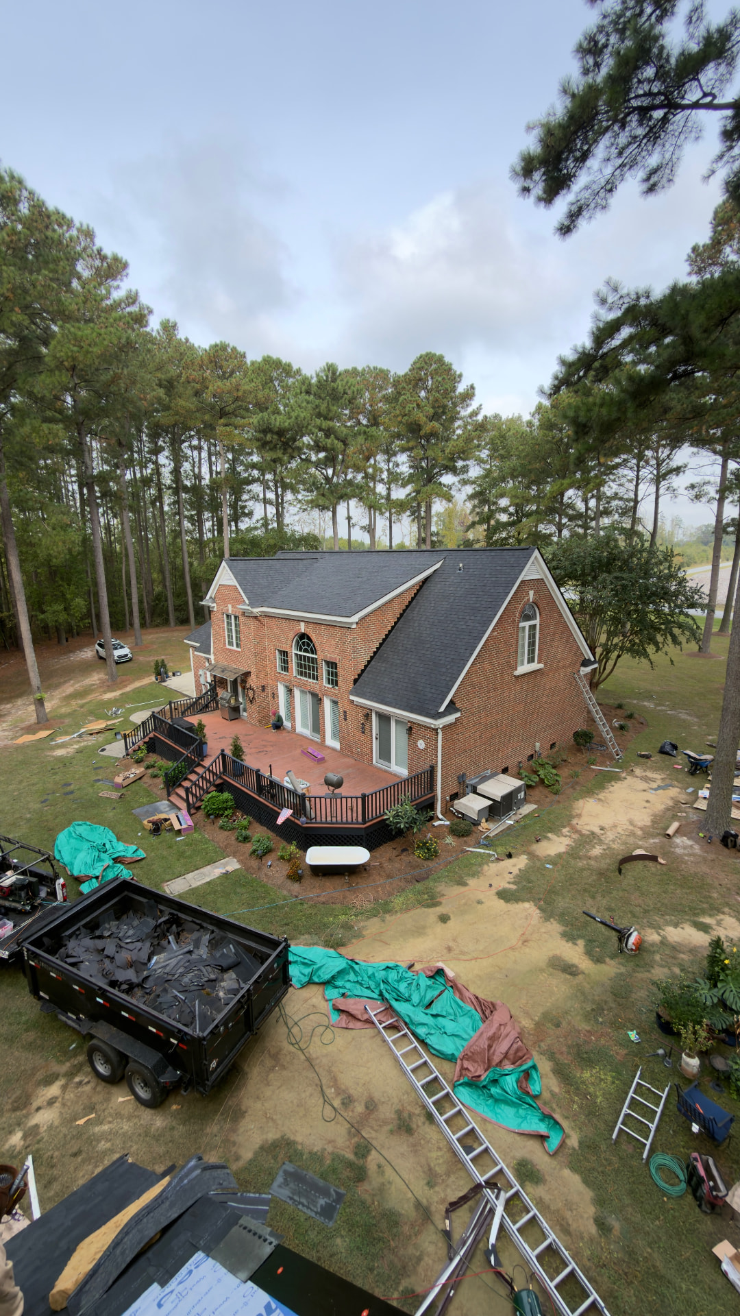 Roof replacement in progress on a red brick home with old shingles loaded in a dump trailer