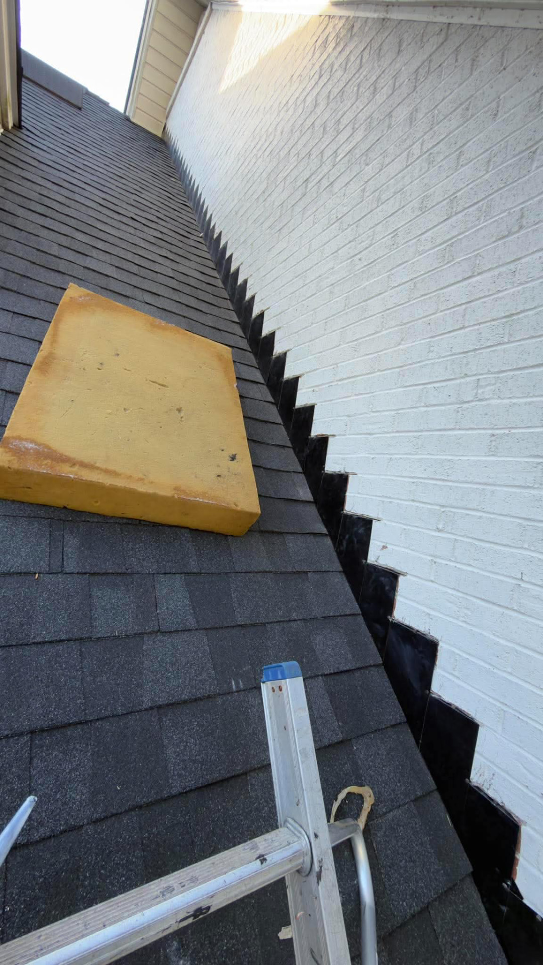 New architectural shingles with step flashing installed against a white brick wall